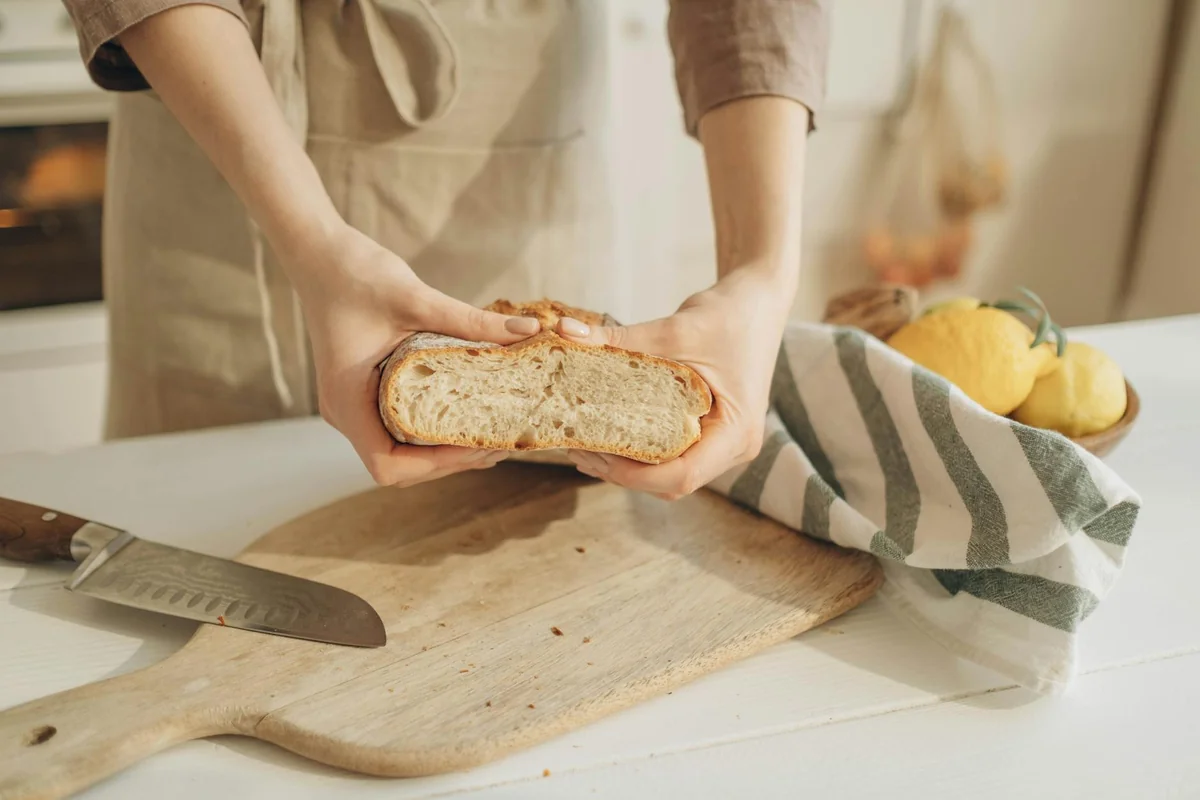 Close-up of hands holding sliced artisan bread on a wooden cutting board with lemons.