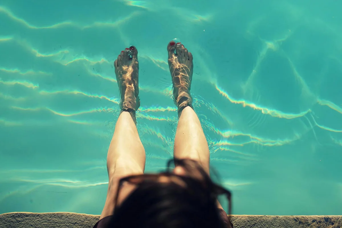 Woman relaxing with feet dipped in a clear pool on a sunny day, capturing a refreshing moment.