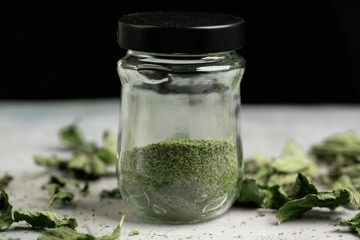 Close-up of a glass jar filled with dried, powdered mint leaves, ideal for culinary use.