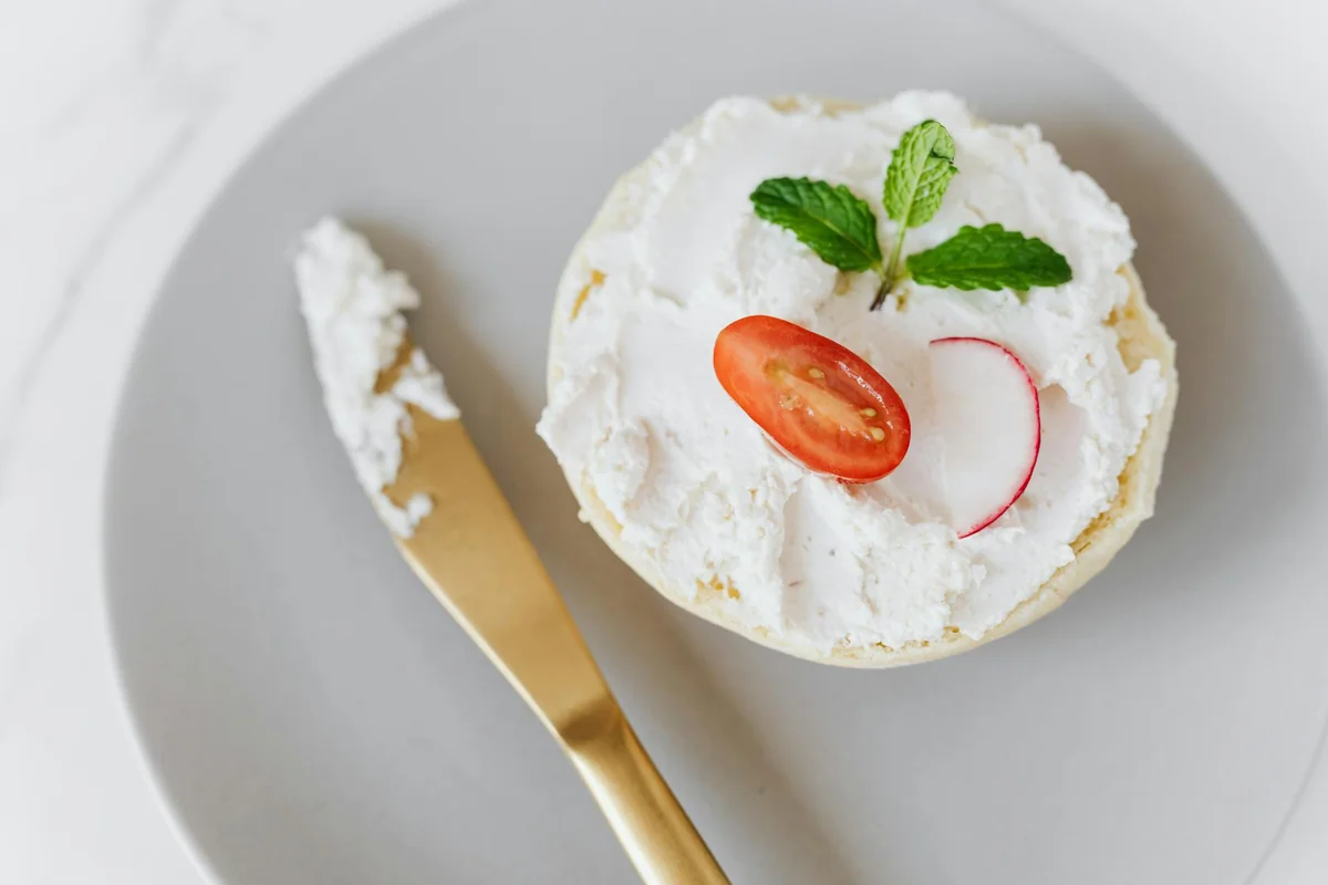 From above of delicious cottage cheese spread on bun decorated with vegetables and mint on round platter with golden knife pl