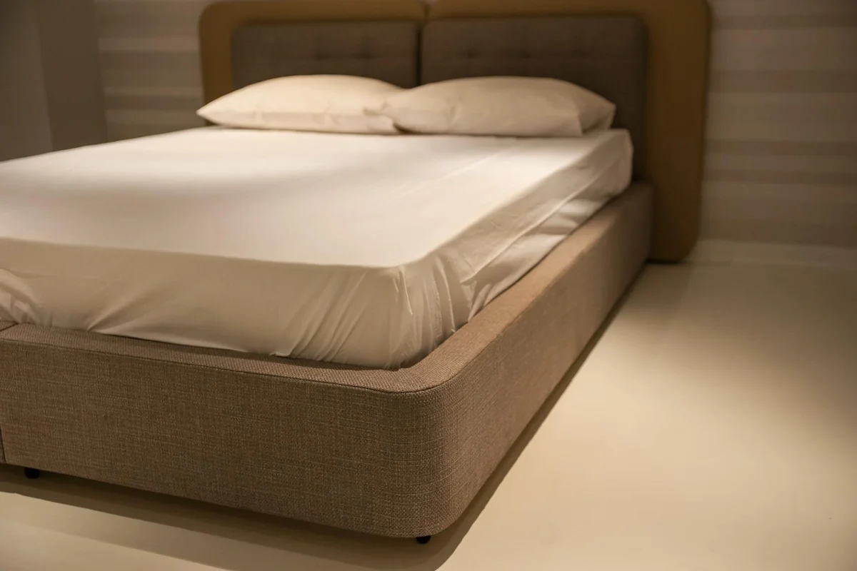 A close-up view of a minimalist bedroom featuring a bed with white linen sheets and plush pillows.