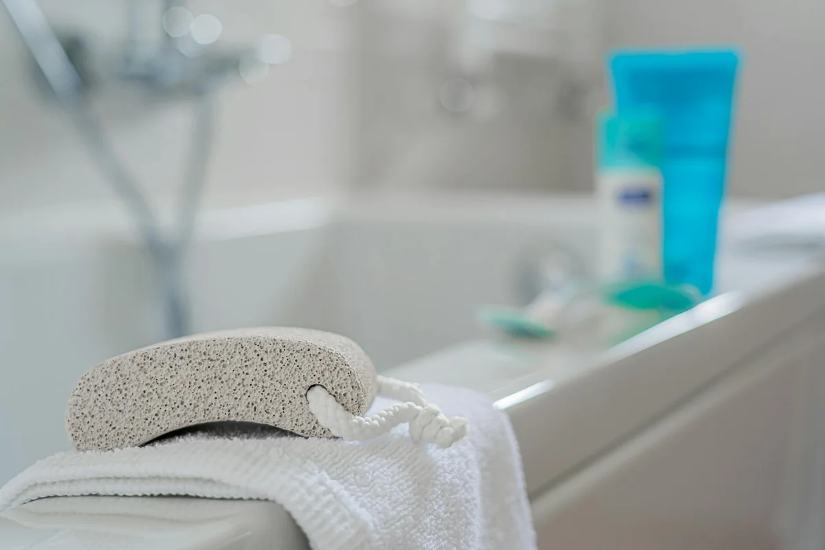 Close-up of a pumice stone and towel by a bathtub with toiletries in a contemporary bathroom setting.