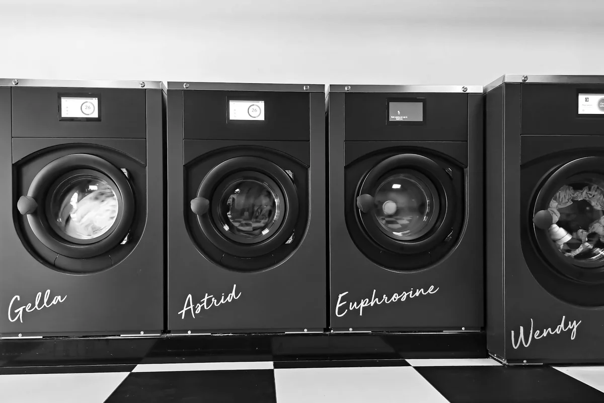 Grayscale image of four modern washing machines in a self-service laundry.
