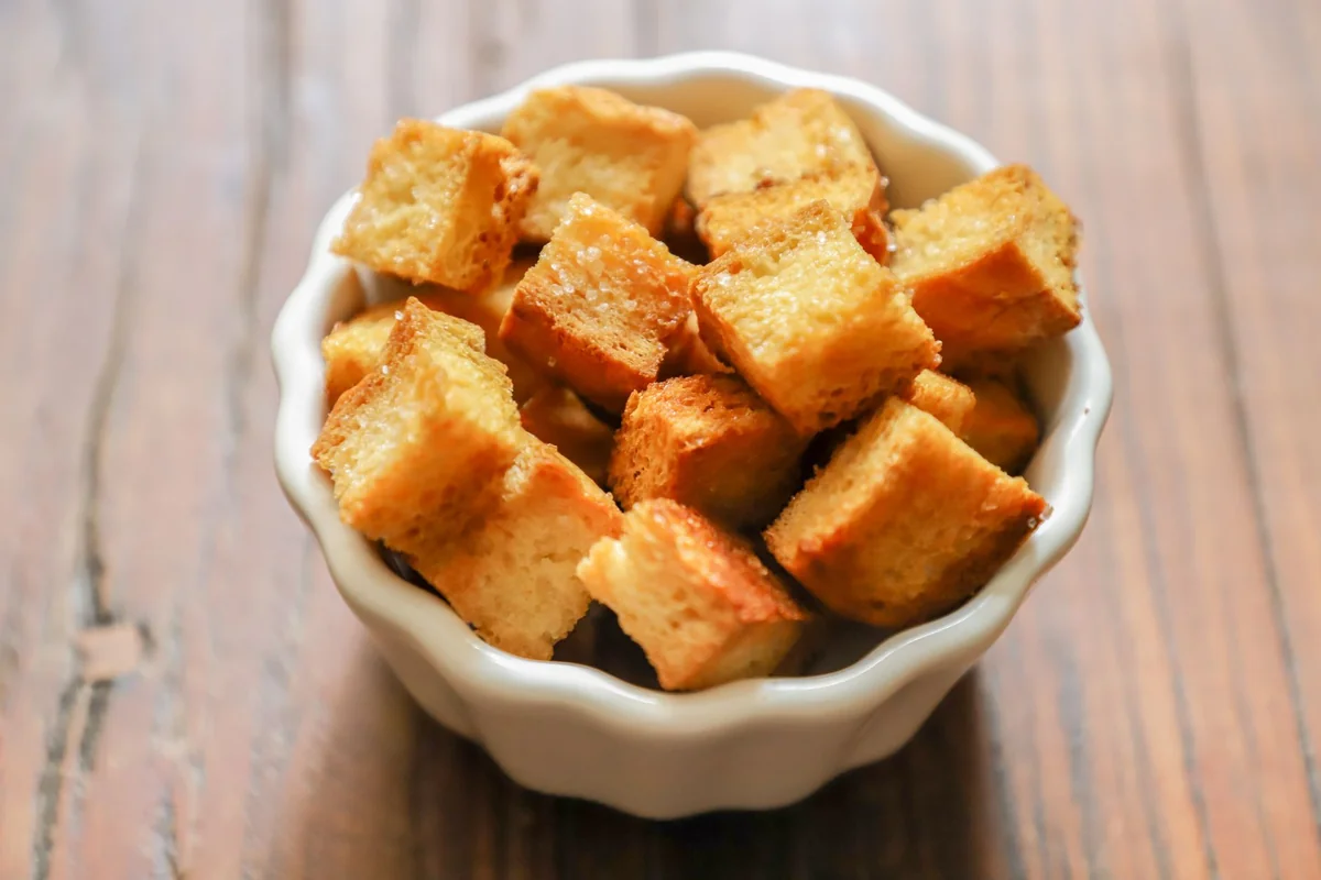 Close-up of golden-brown croutons in a white ceramic bowl on a rustic wooden table.