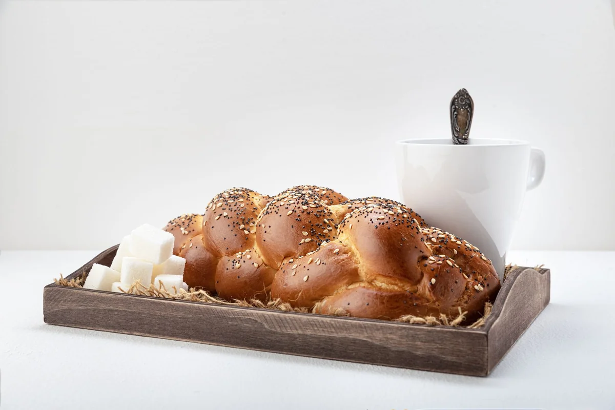 Delicious freshly baked challah bread on a wooden tray with a mug of coffee.