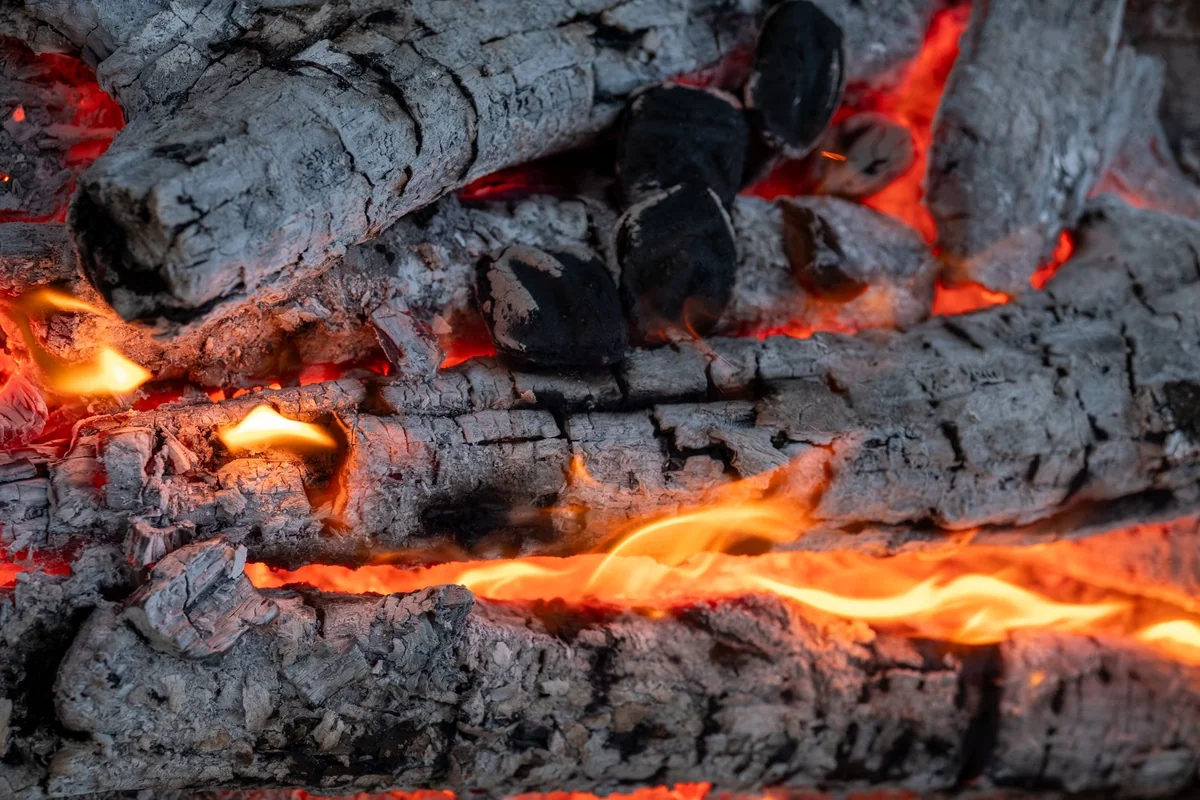 A detailed view of burning firewood with bright flames and glowing embers.