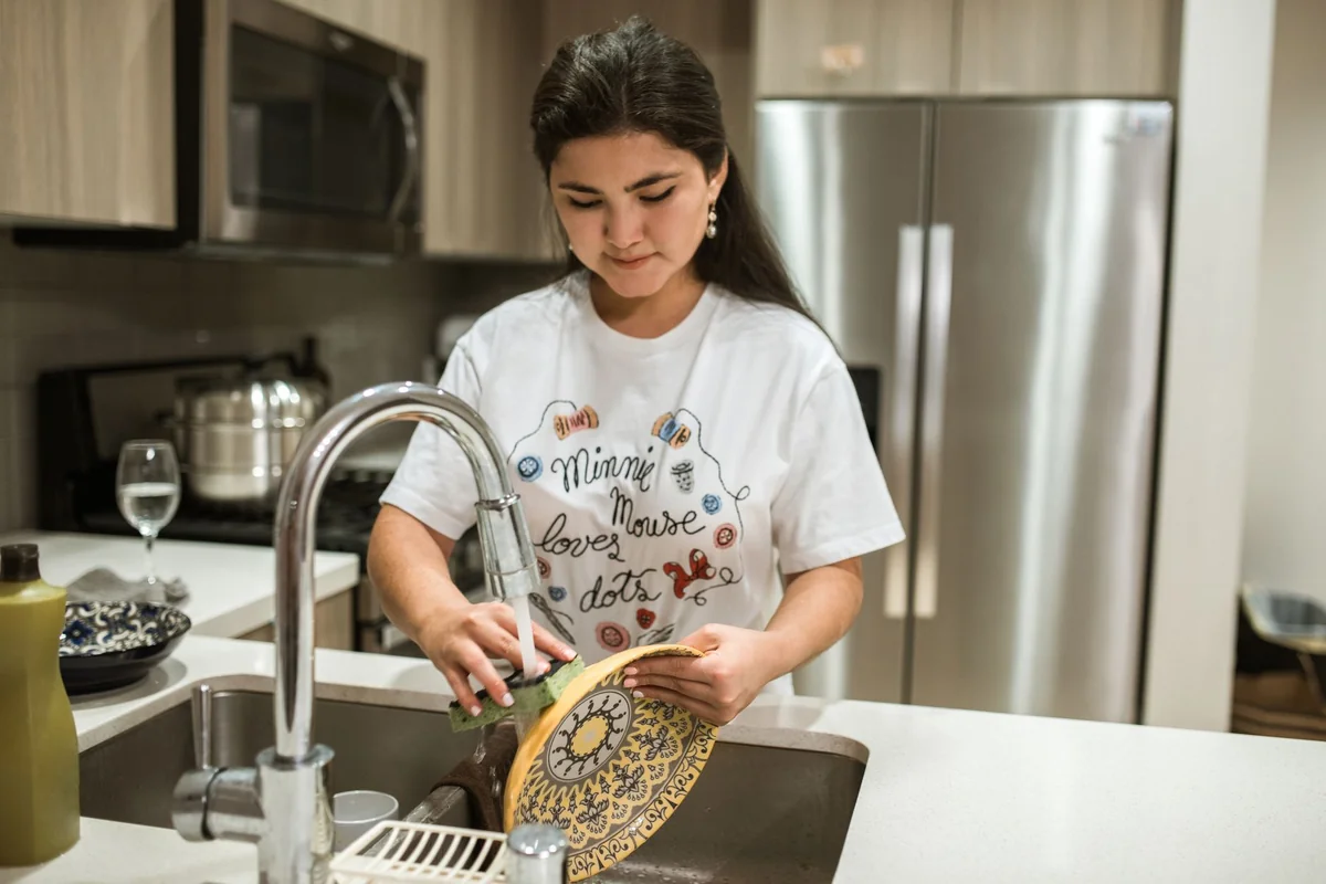 Young woman washing a plate in a modern kitchen sink, showcasing everyday household chores.