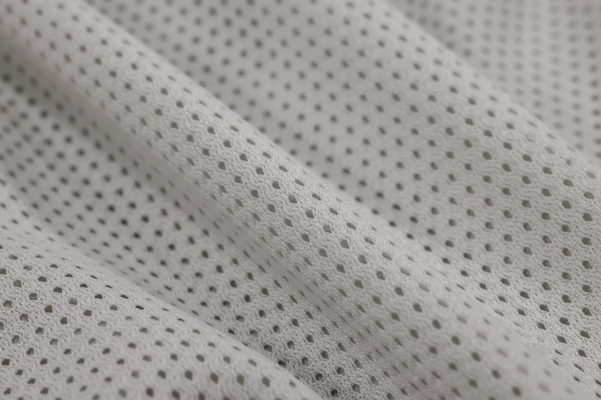 Detailed close-up of soft white textured fabric with small holes, perfect for design and textiles.