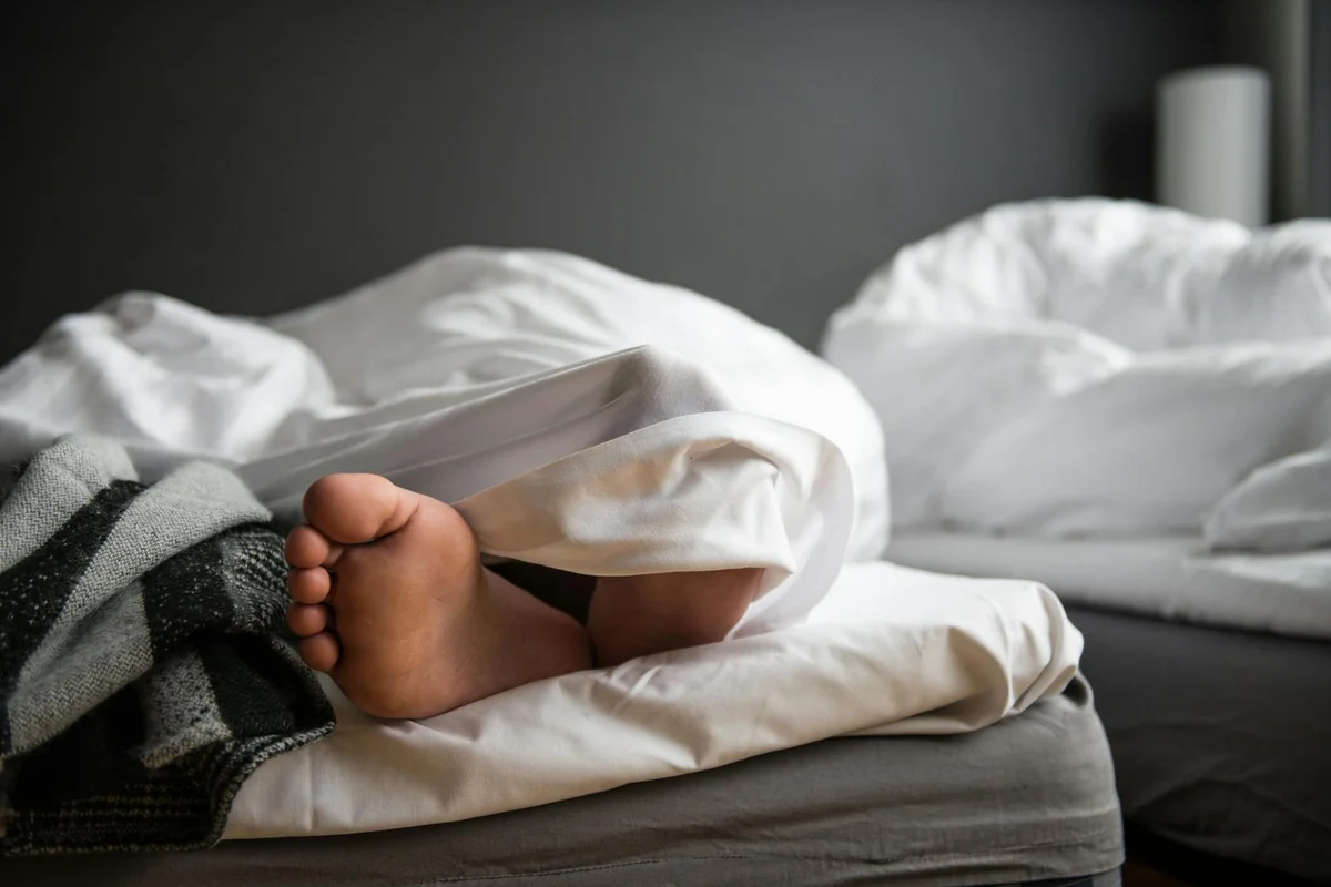 A close-up of a bare foot poking out from under a soft duvet in a modern bedroom.