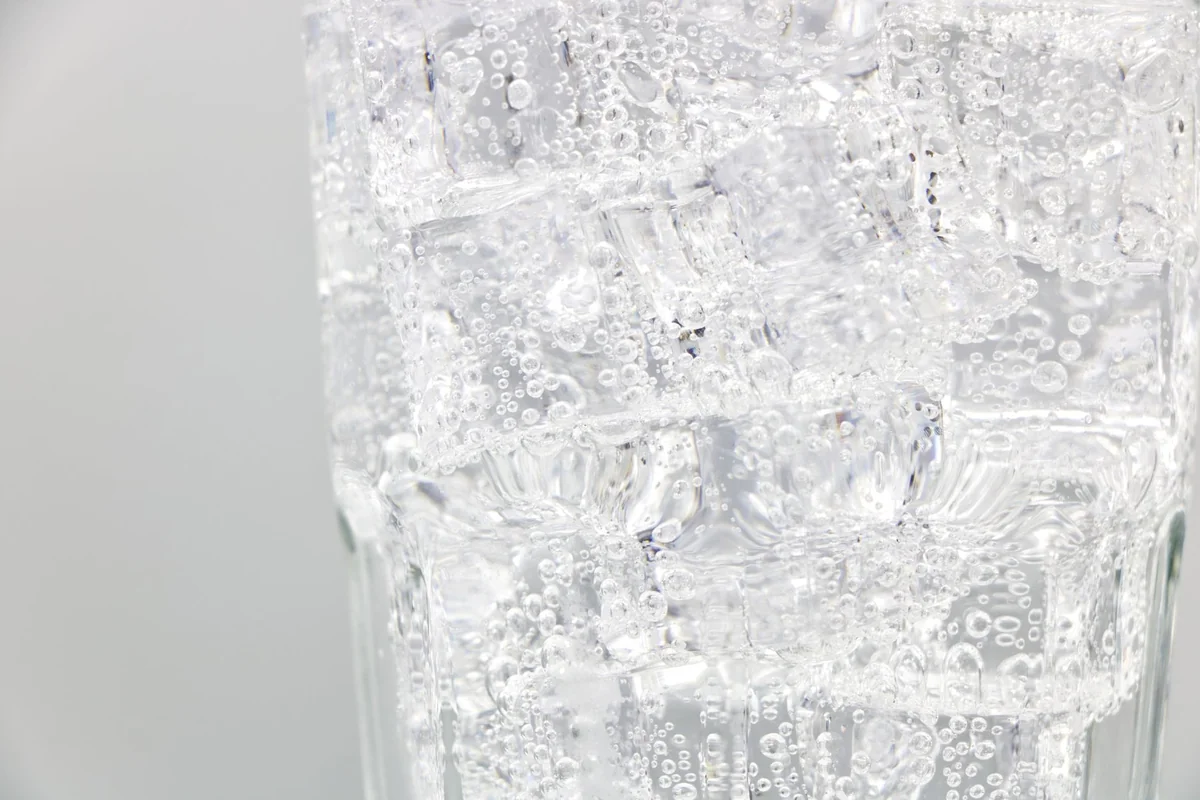 Refreshing sparkling water with ice cubes in a clear glass, close-up view.