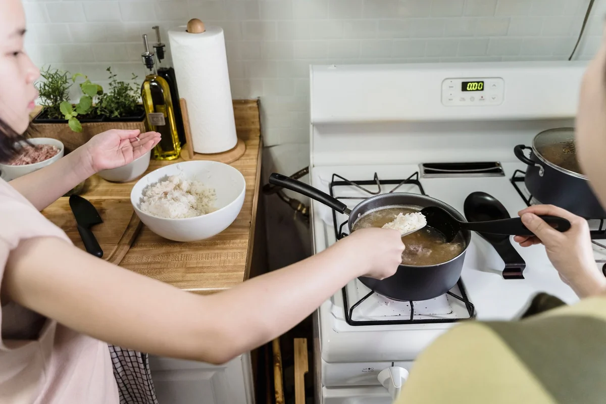 A mother and daughter cook rice together on a stove, fostering family bonding in the kitchen.