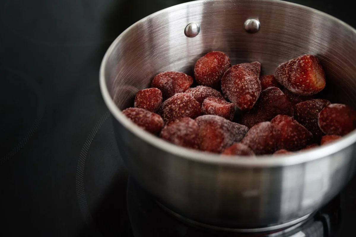 Closeup of glow metallic bowl with frozen strawberry on black smooth stove surface