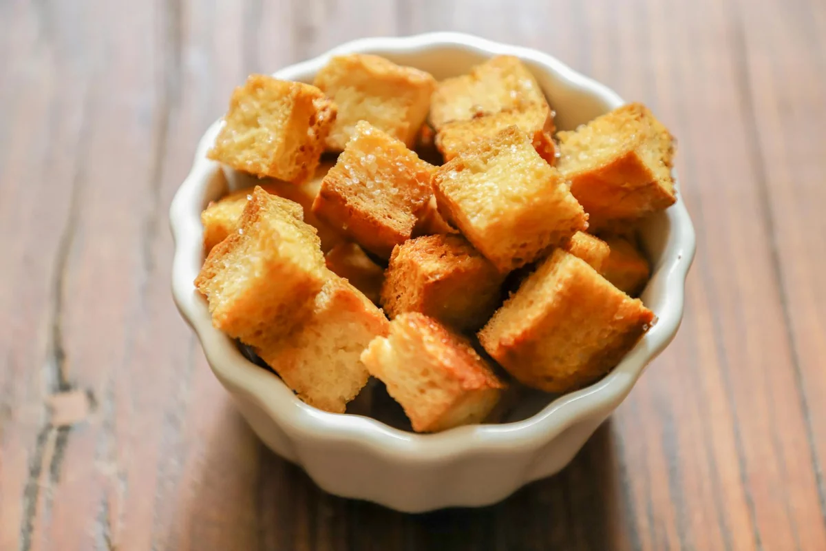 Close-up of golden-brown croutons in a white ceramic bowl on a rustic wooden table.