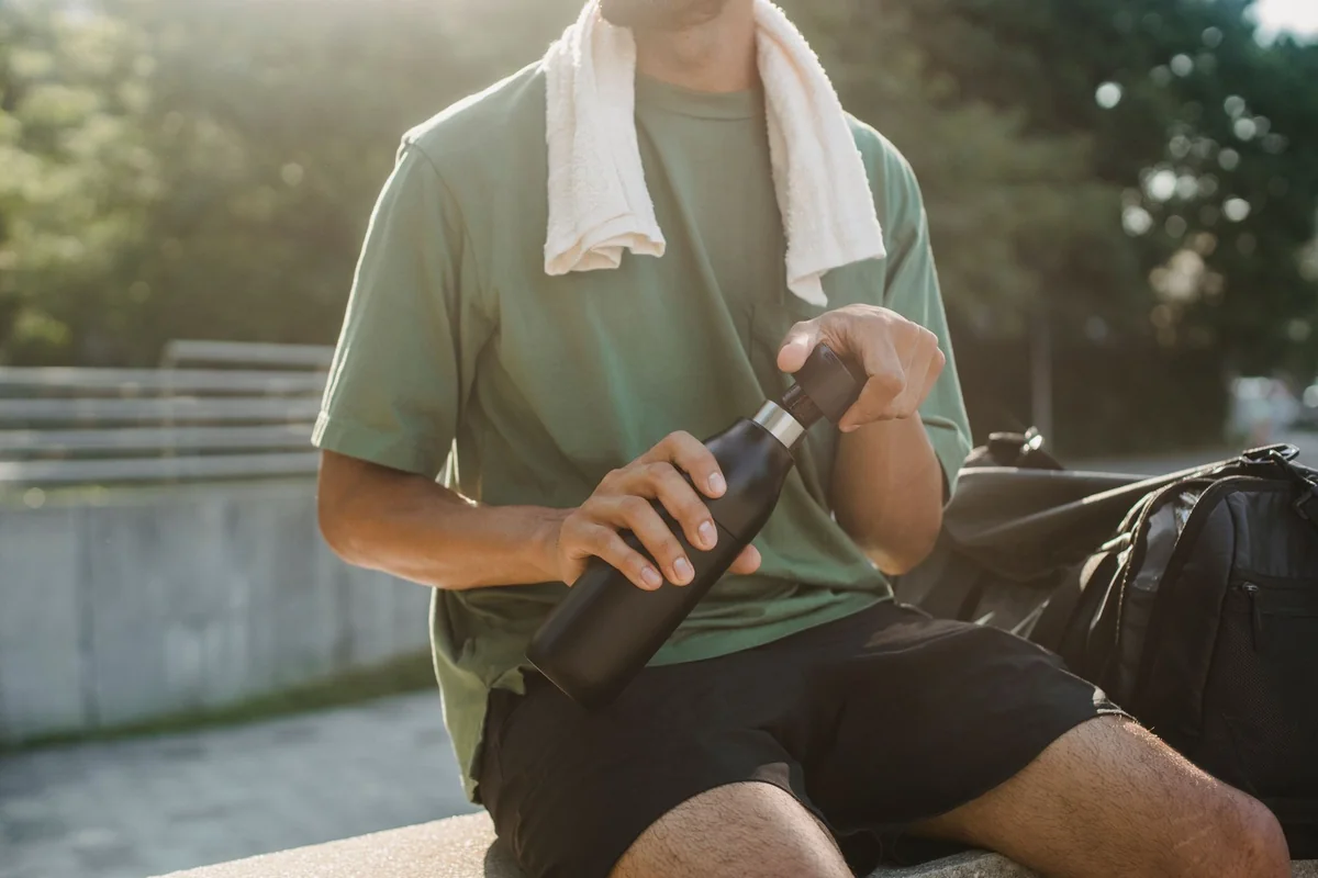 Close-up of a man sitting outdoors with a reusable water bottle and towel.