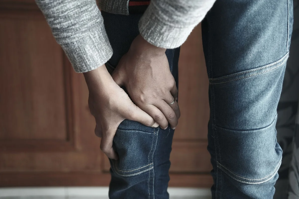 A person holds their knee in denim jeans, showing a sense of tension.