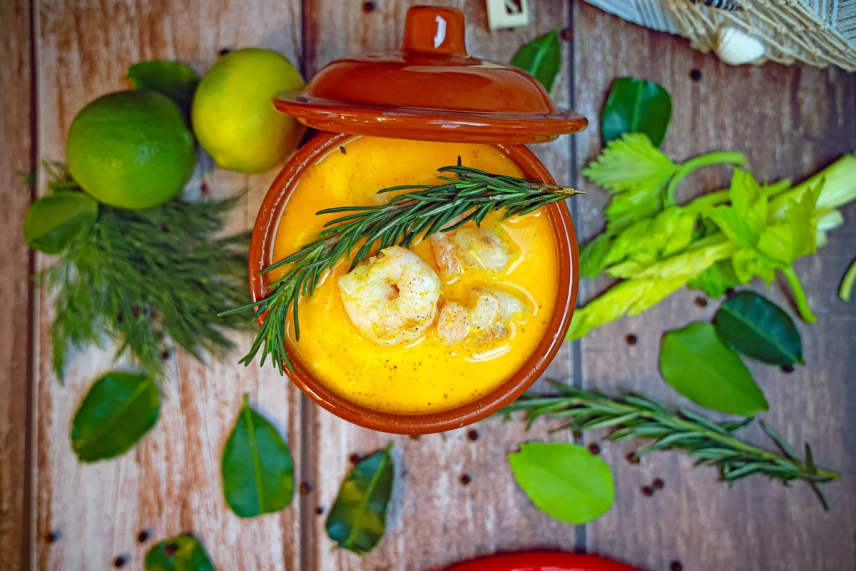 A top-down view of a creamy shrimp bisque garnished with rosemary, surrounded by fresh herbs.