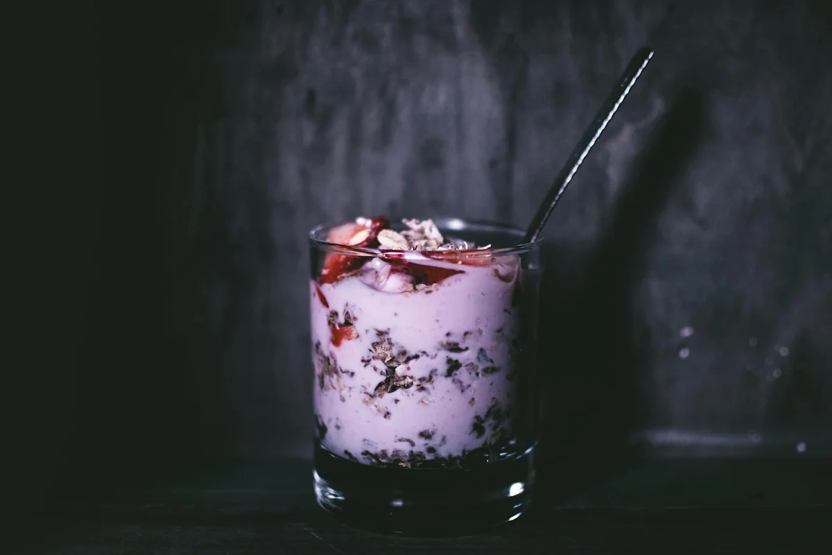 Dark, moody close-up of a delicious yogurt parfait with granola and berries in a glass.
