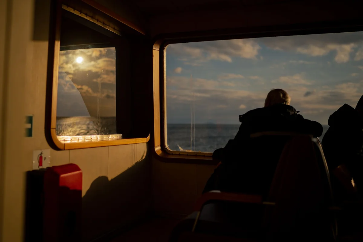 A person gazes out the ferry window at the sea during sunset, creating a serene mood.