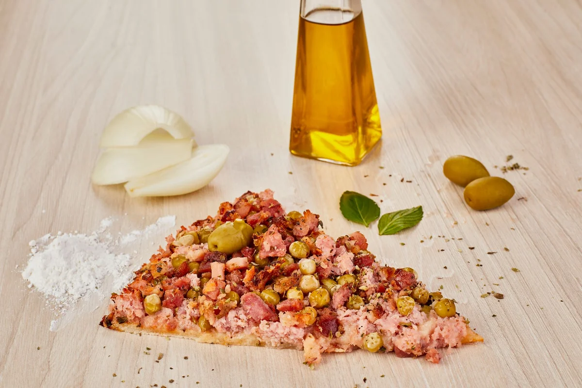Close-up of Italian pizza slice with olives, onions, and oil on a wooden surface.