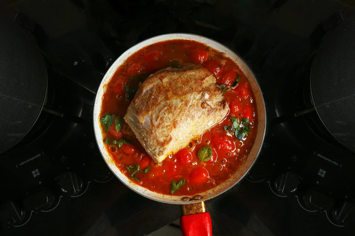 A savory roast beef cooked in rich tomato sauce with herbs, atop a stovetop.