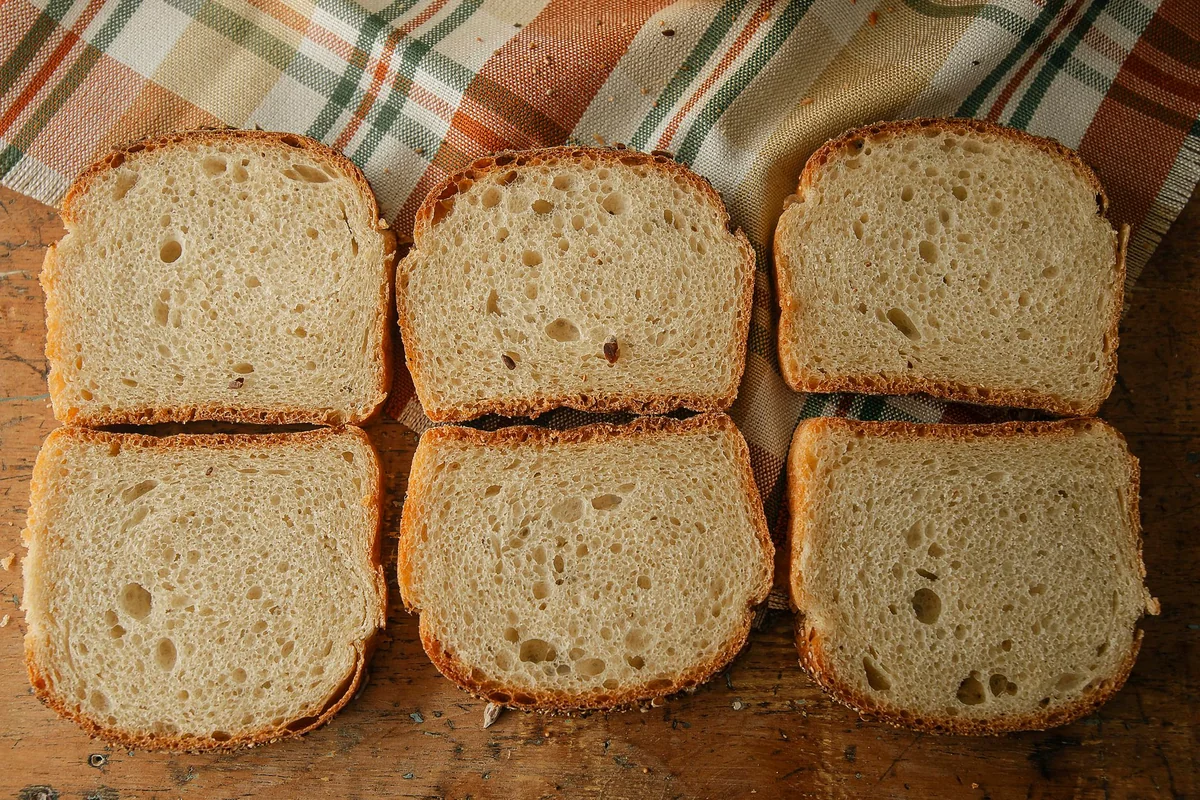 Six slices of fresh bread arranged on a wooden table with a plaid cloth backdrop.