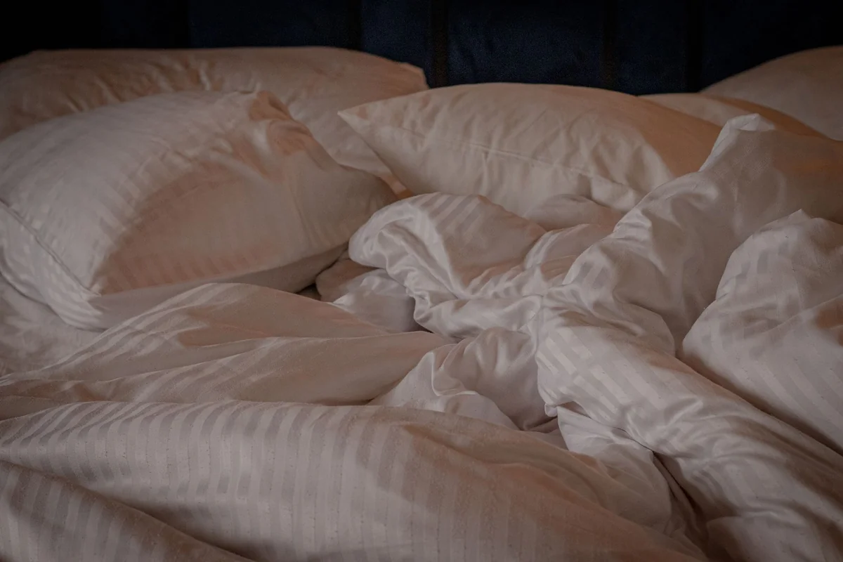 A comfortable and inviting bed with white pillows and a crumpled duvet, perfect for a relaxing setting.