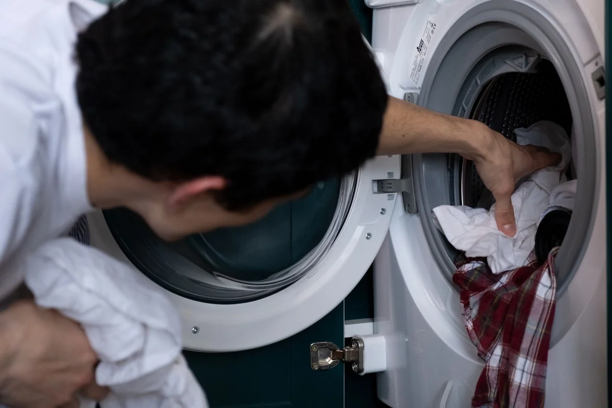 Close-up of a man placing clothes into a washing machine during household chores.