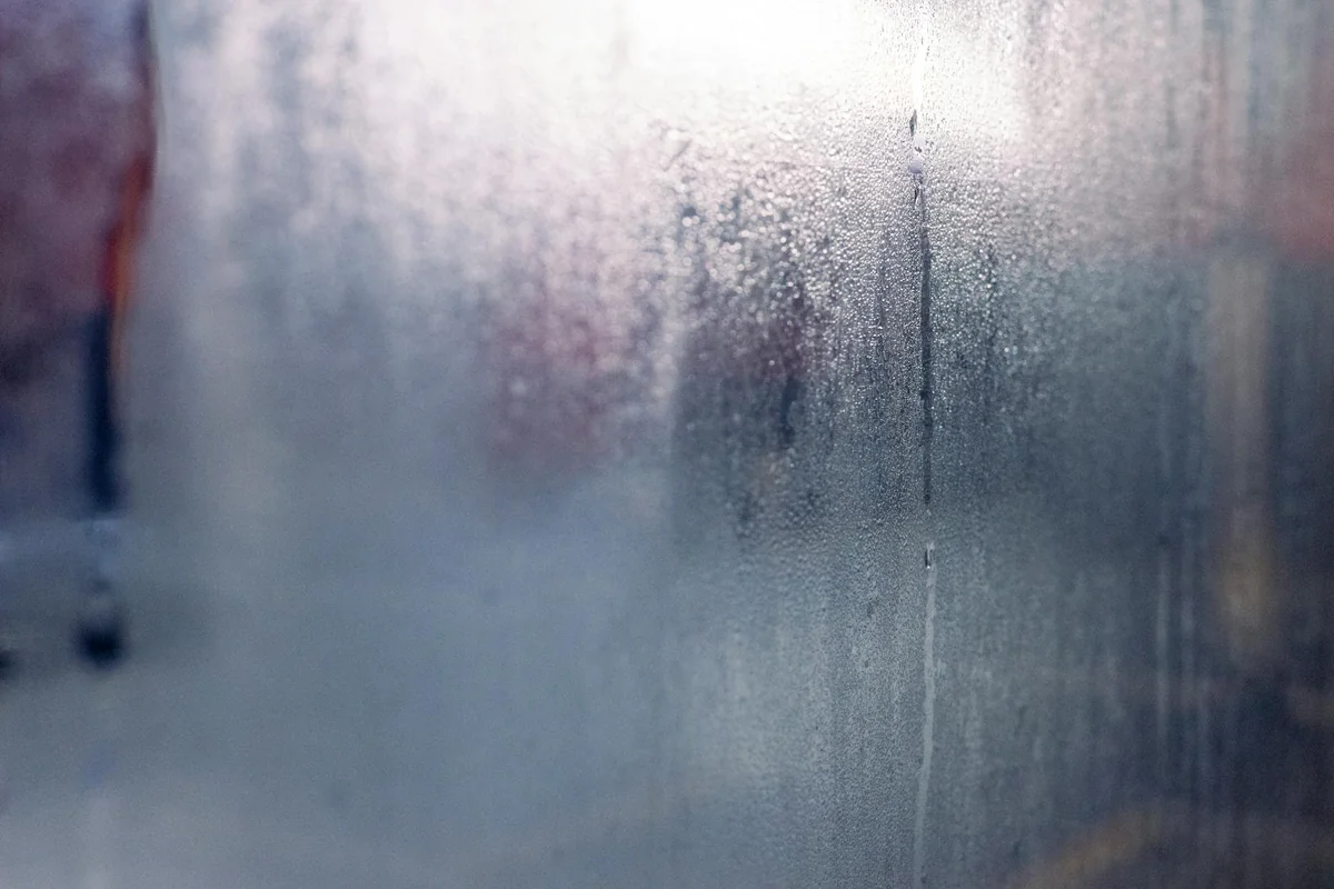 Moisture droplets on a foggy window create a mysterious and serene atmosphere.